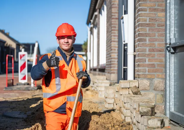 Construction worker in high-visibility safety gear inspecting brick building foundation for energy infrastructure project.