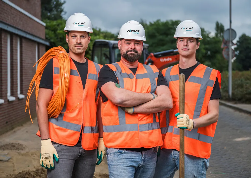 Three Circet Energy workers wearing high-visibility vests and safety helmets, posing with construction tools on-site.