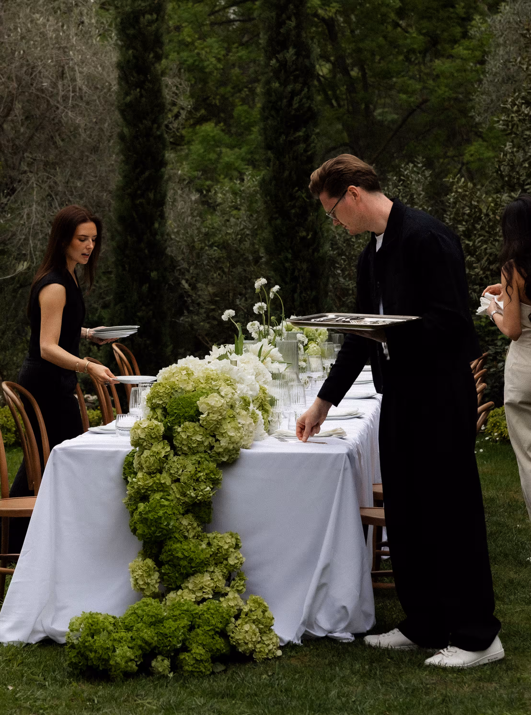 Two members of the catering team dressing a long table, its runner a cascade of green hydrangea.