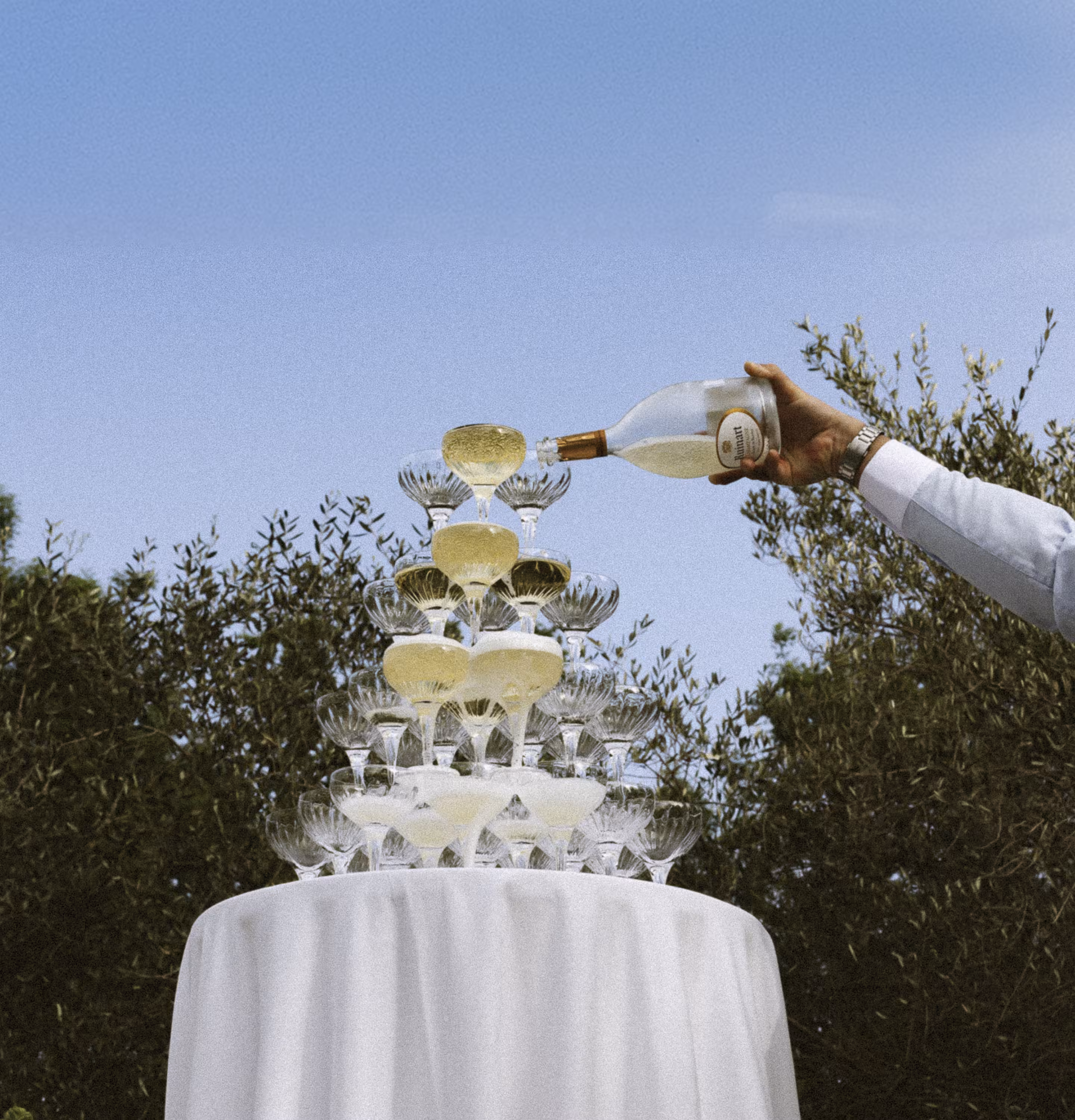 A champagne tower catching the last of the daylight, poured glass by glass beneath the trees.