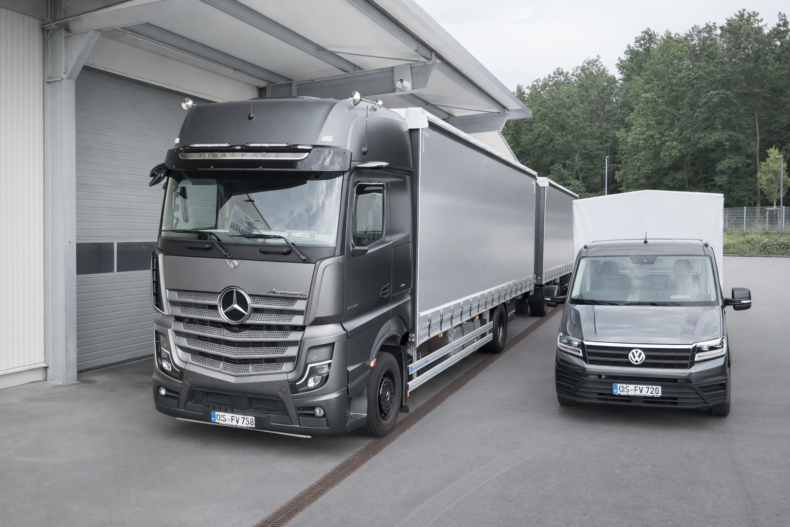 Gray Mercedes-Benz Actros truck and a gray Volkswagen van parked side by side outside a warehouse.