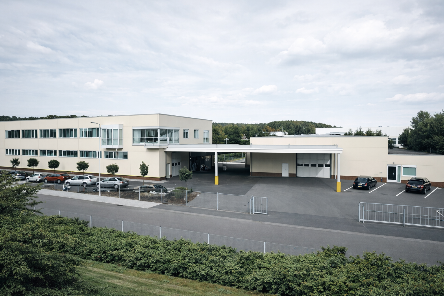 Modern commercial building with a parking area and several parked cars under an overcast sky.