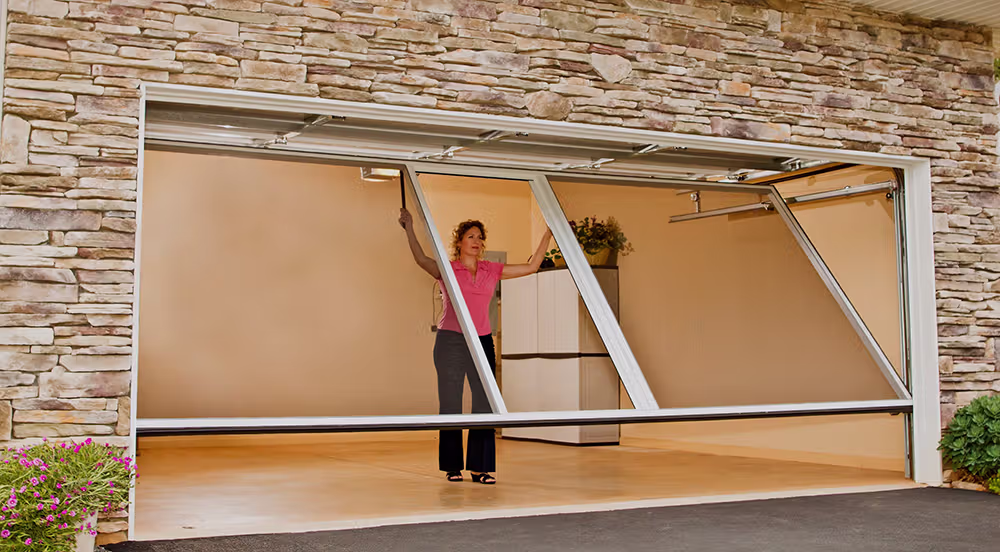Woman in a pink shirt opening a modern garage door with stone facade around it.