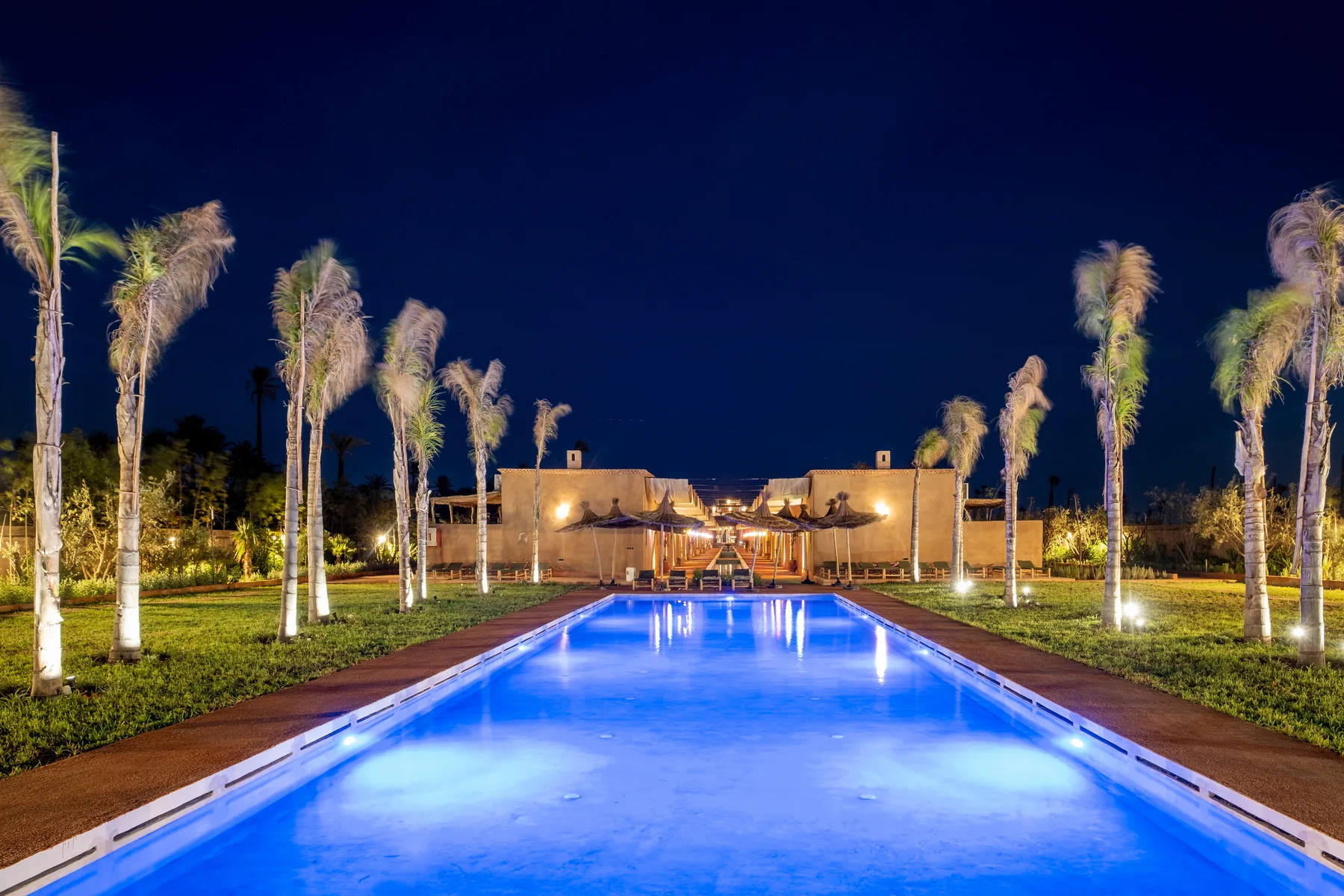 Villa Moira, celebration villa in the Palmeraie, Marrakech, heated lagoon pool illuminated at night. The Marrakech Curator.