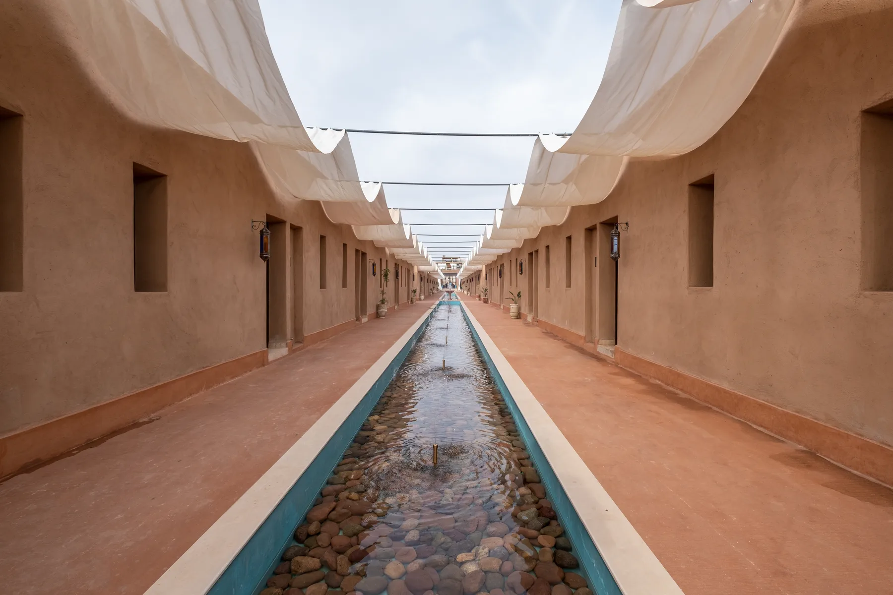 Villa Moira, celebration villa in the Palmeraie, Marrakech, water-garden walkway under white canopies. The Marrakech Curator.