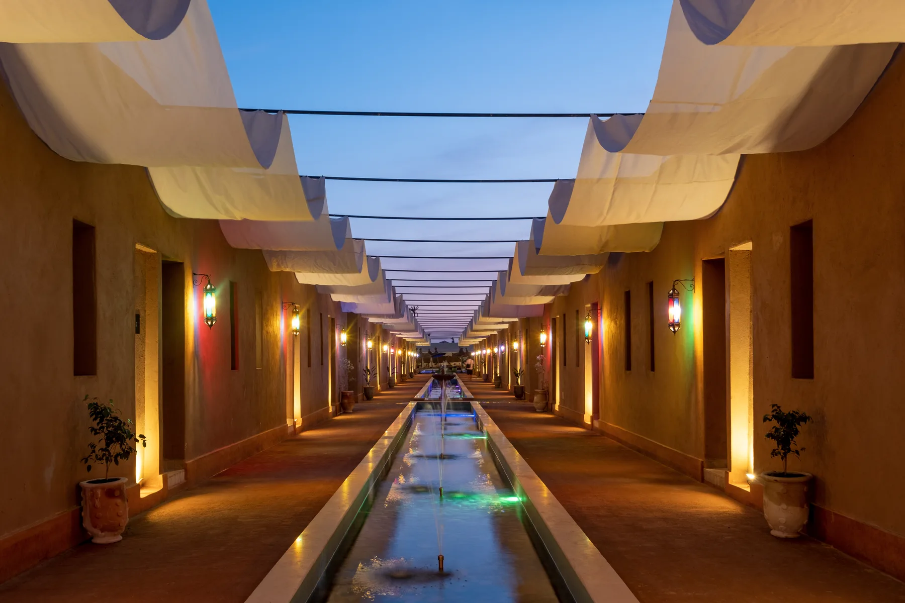 Villa Moira, celebration villa in the Palmeraie, Marrakech, lantern-lit walkway in the evening. The Marrakech Curator.