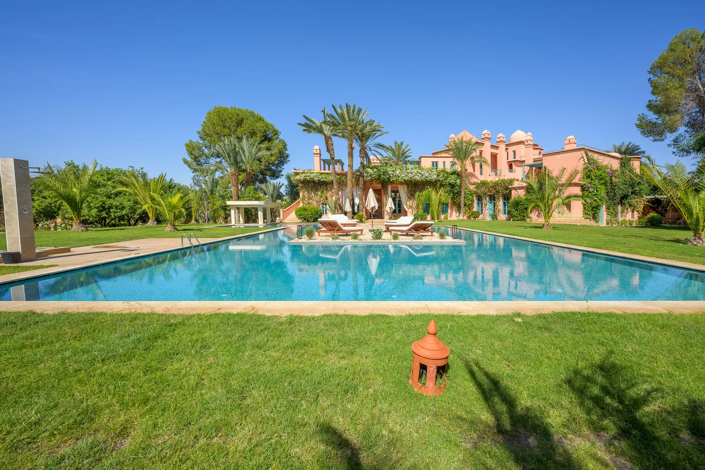 Villa Calypso, private villa rental in the Palmeraie, Marrakech: swimming pool and lawn in front of the pink villa
