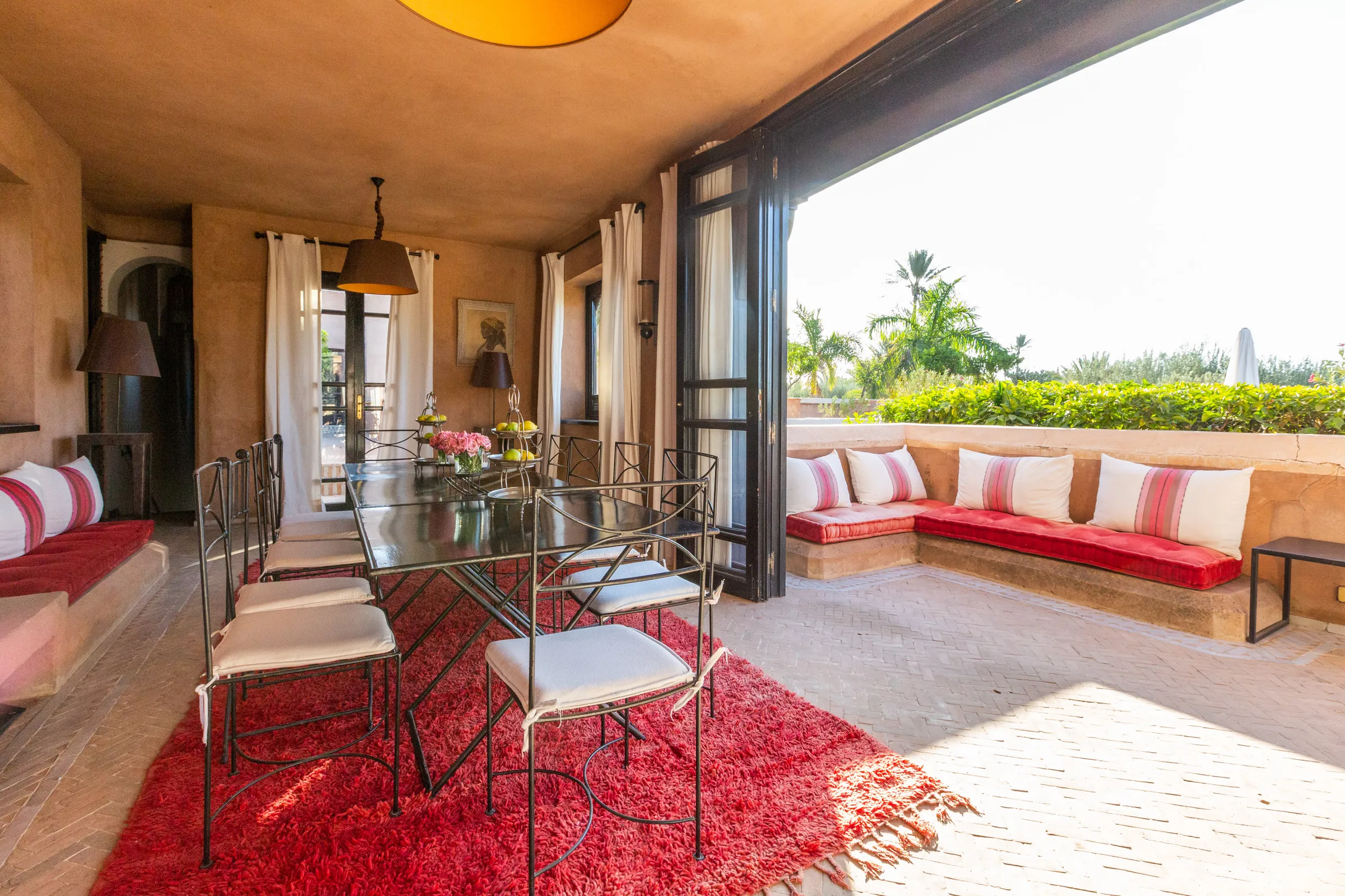 Villa Amalthea, private villa rental in the Palmeraie, Marrakech: covered veranda with dining table and red banquettes