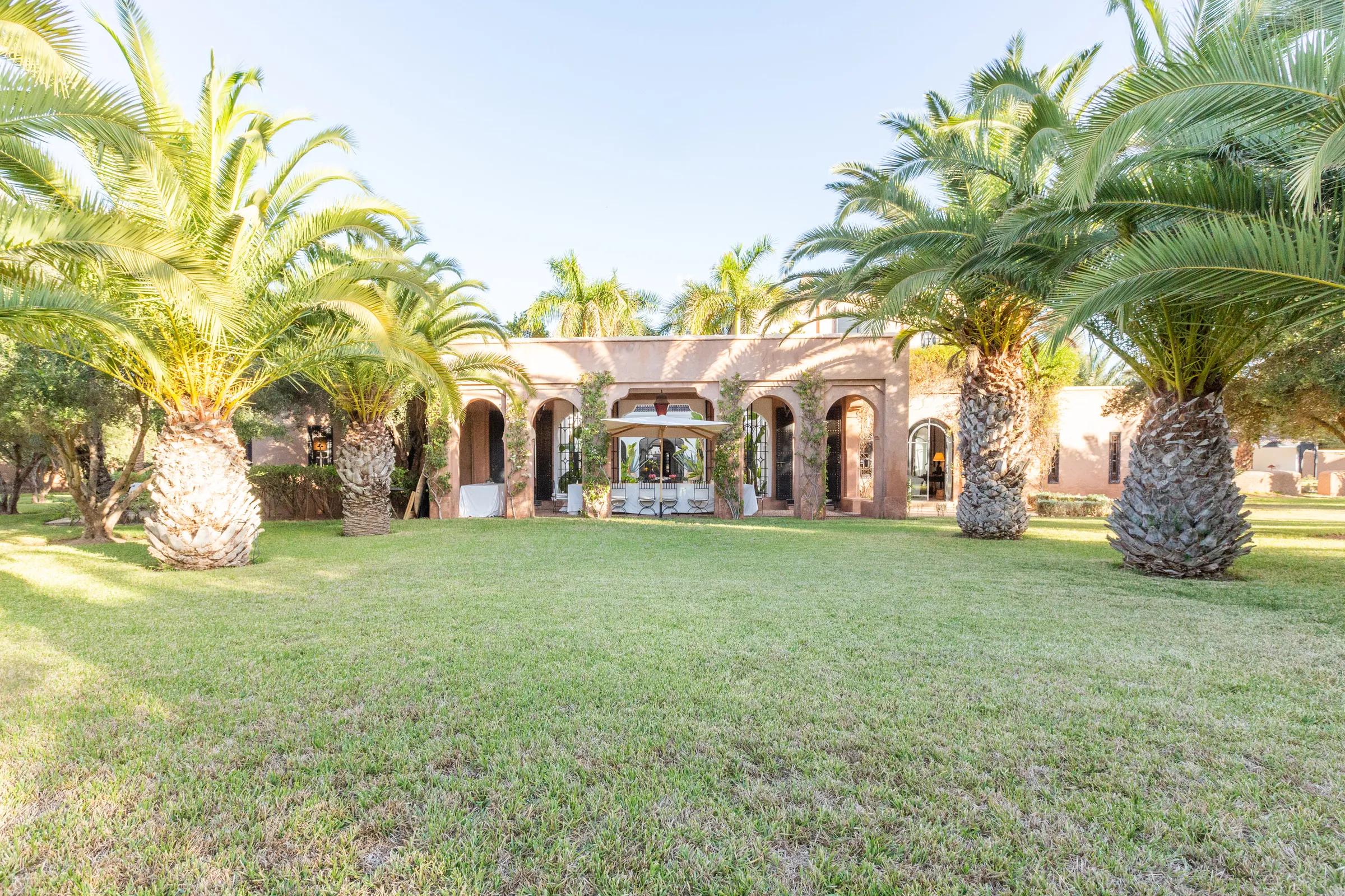 Villa Amalthea, location de villa privée dans la Palmeraie à Marrakech : pelouse et palmiers devant la villa à arcades