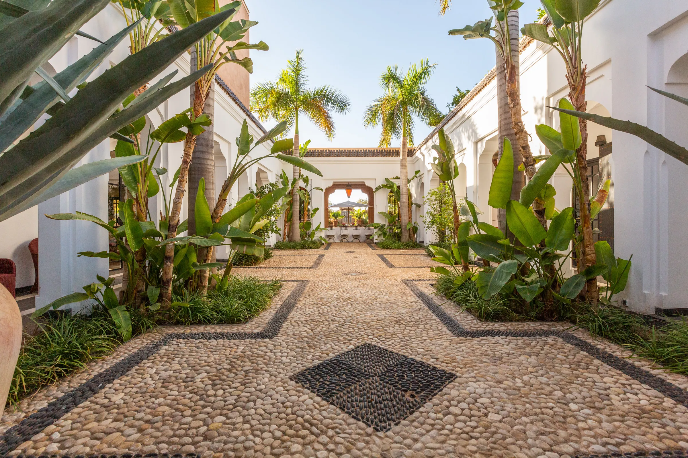 Villa Amalthea, private villa rental in the Palmeraie, Marrakech: white courtyard with pebble mosaic paving and tropical plants