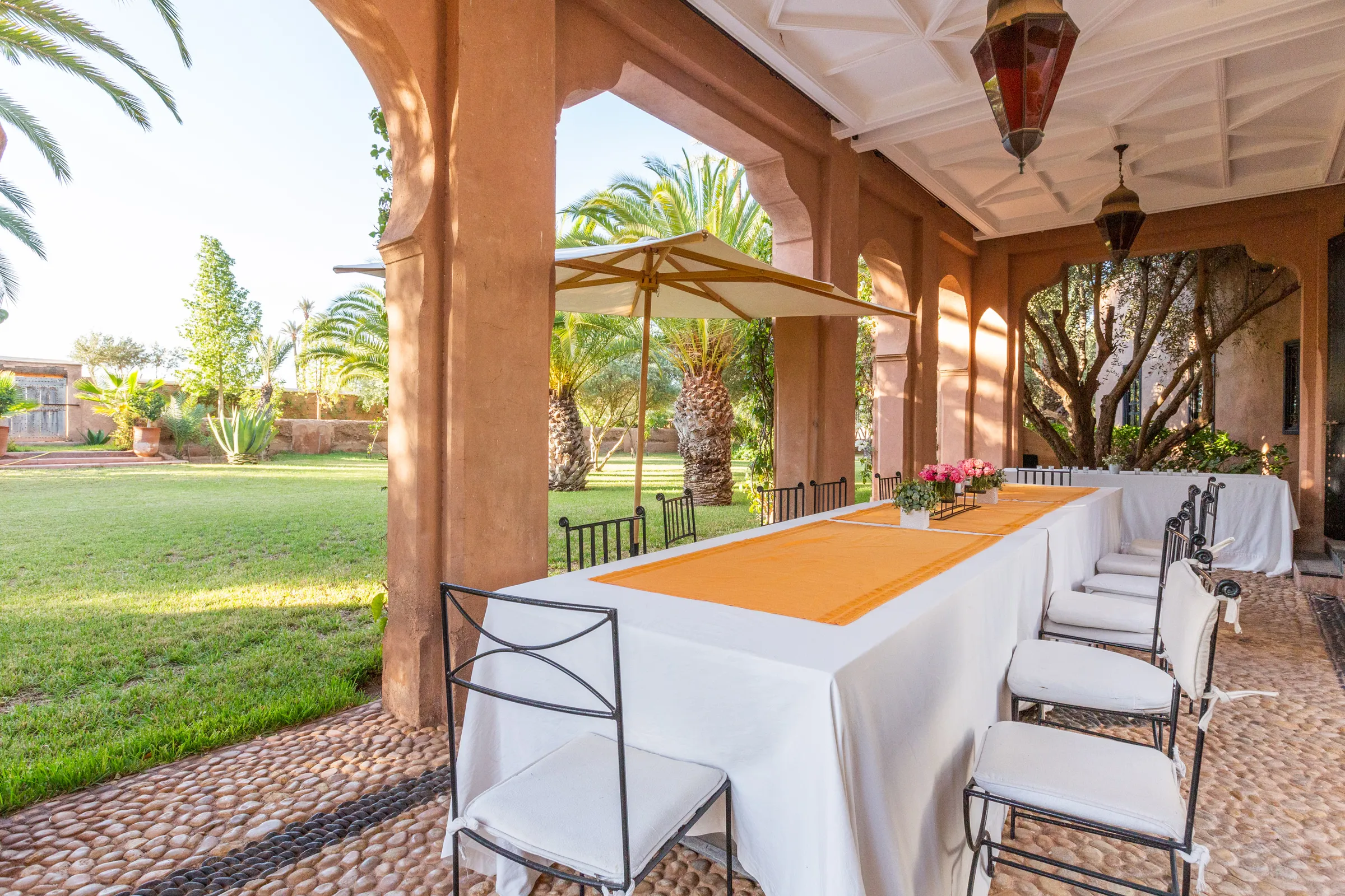Villa Amalthea, private villa rental in the Palmeraie, Marrakech: long outdoor dining table under the arcade facing the lawn