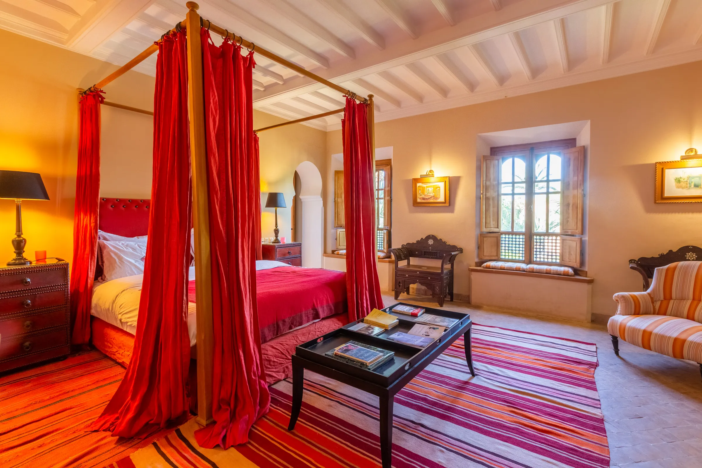 Villa Amalthea, private villa rental in the Palmeraie, Marrakech: bedroom with red-curtained four-poster bed