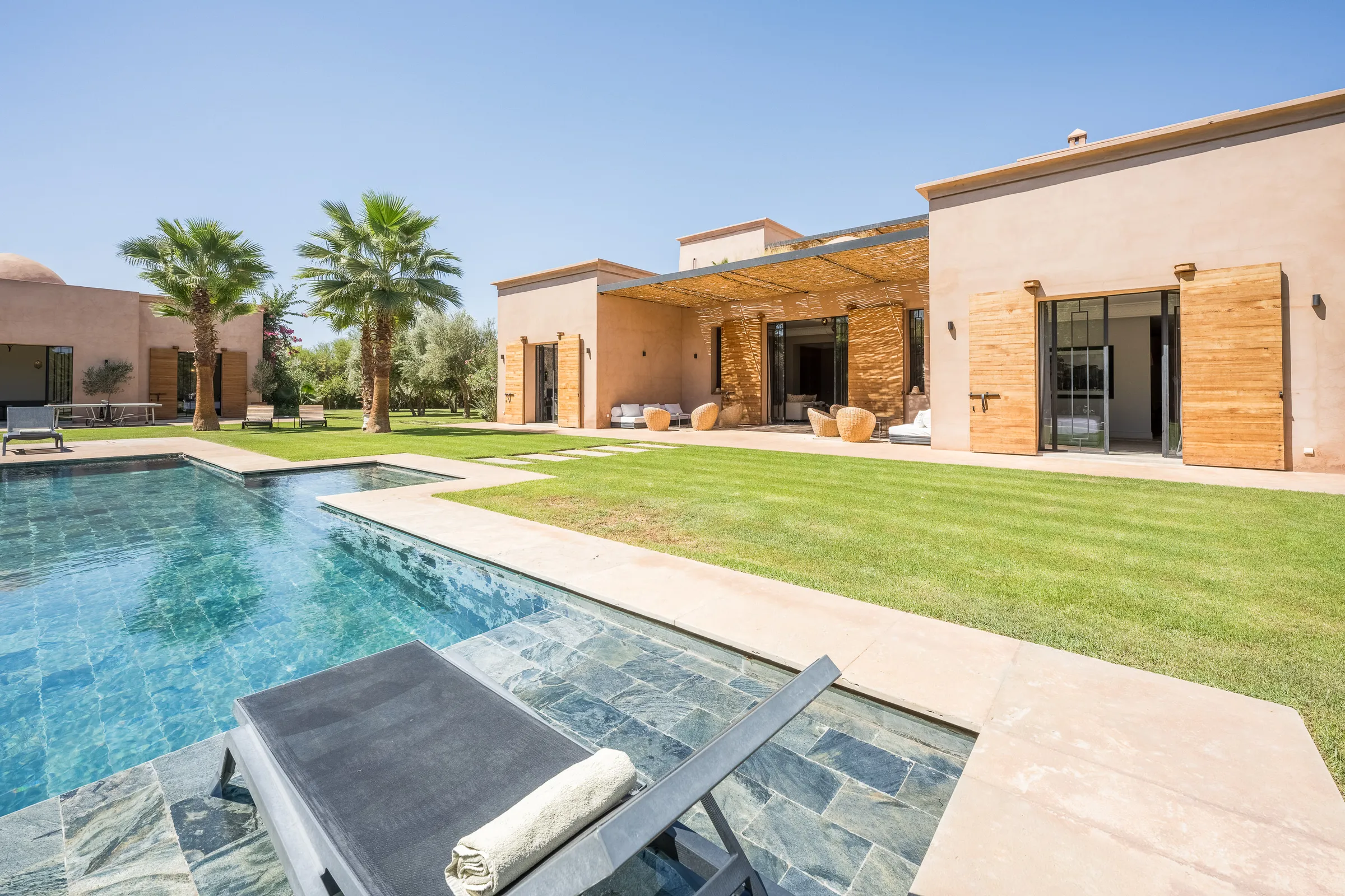 Villa Elara, private villa rental on the Route de Ouarzazate, Marrakech: pool, lawn and villa facade with wooden shutters