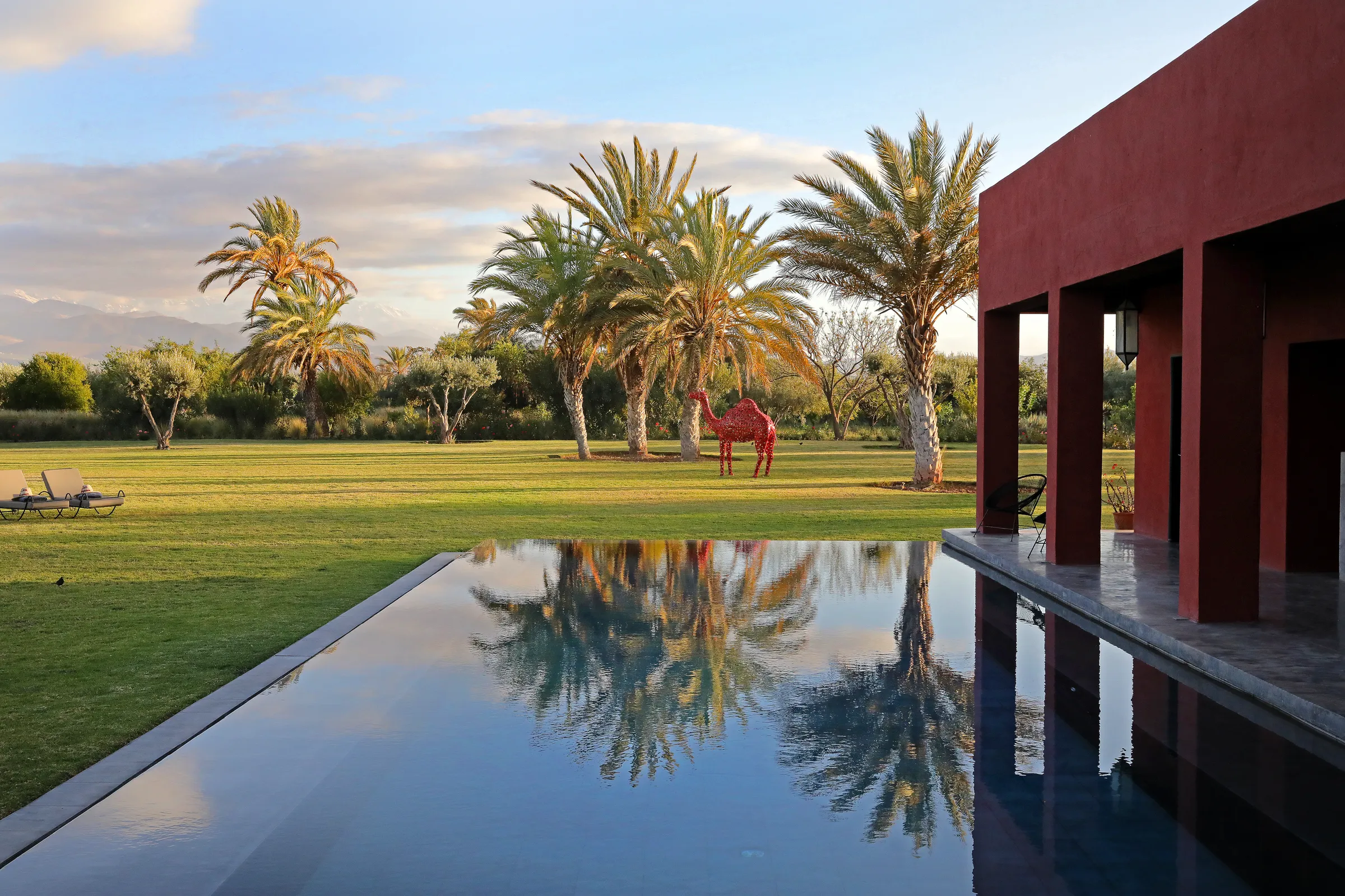 Villa Iliana, private villa rental on the Route de l'Ourika, Marrakech: pool reflecting palm trees beside the red villa