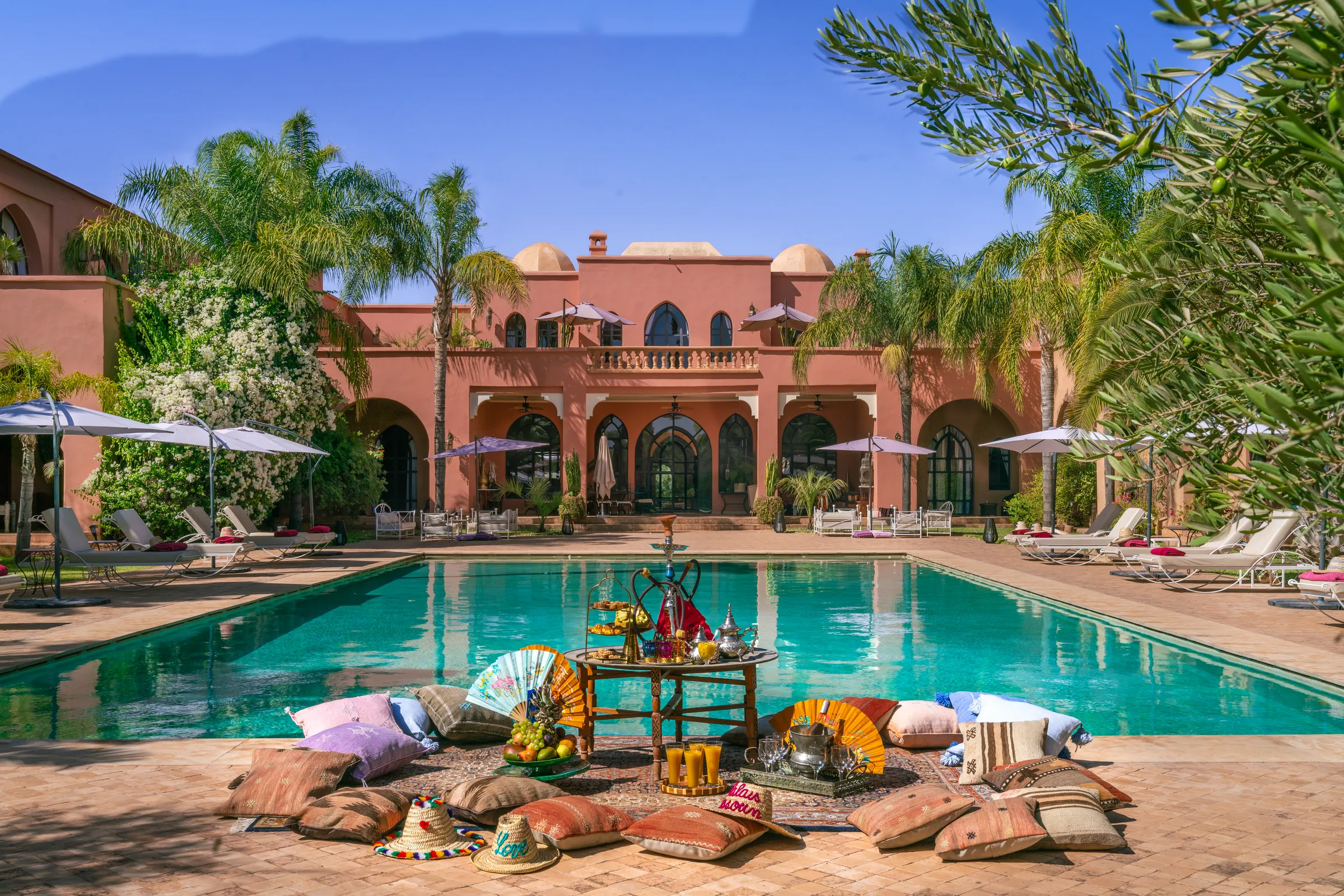 Villa Lyra, private villa rental in Ouled Hassoune, Marrakech: swimming pool with floor cushions in front of the pink palace