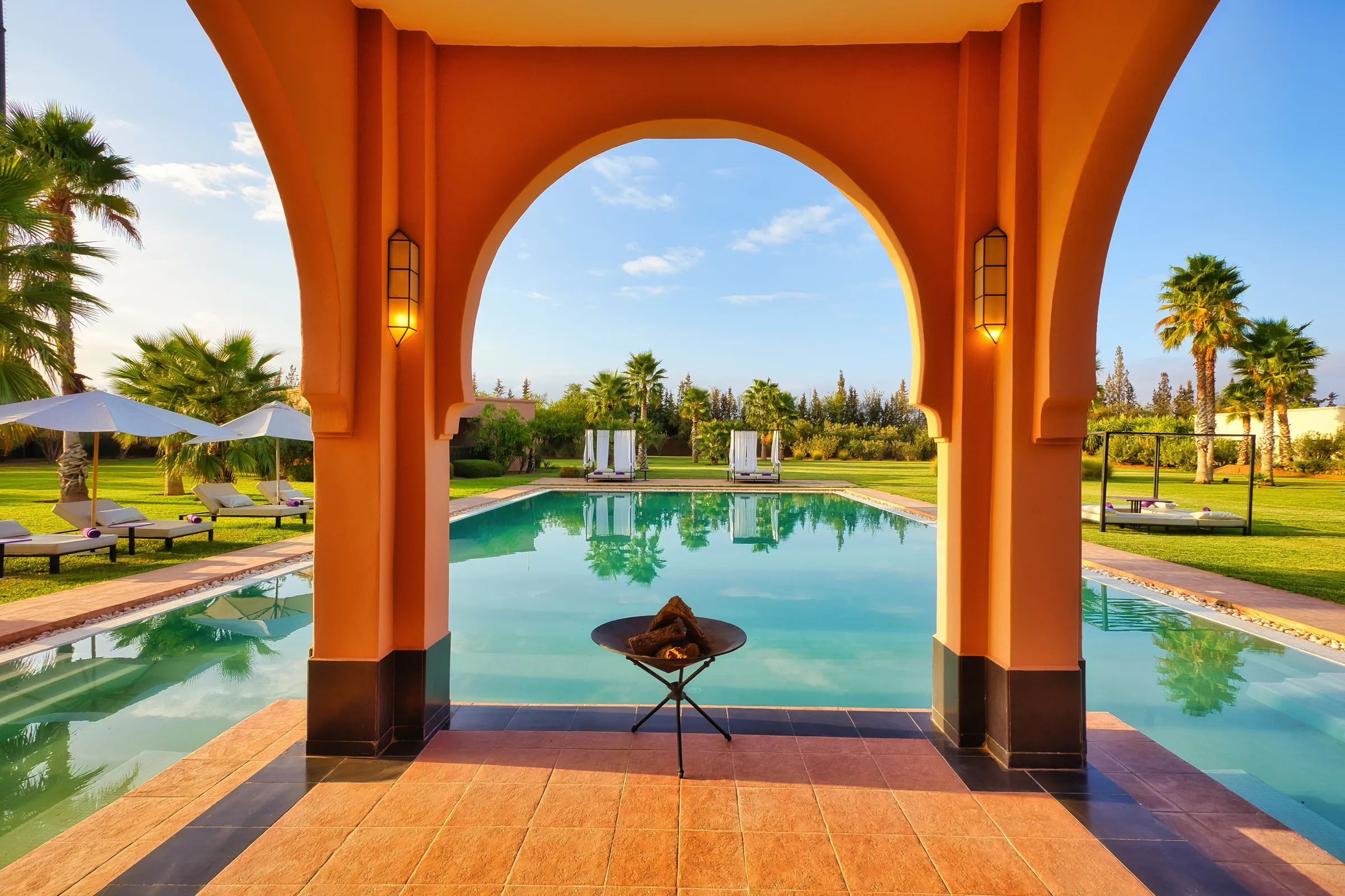 Villa Theia, private villa rental on the Route de l'Ourika, Marrakech: Moorish arch framing the pool and a fire bowl
