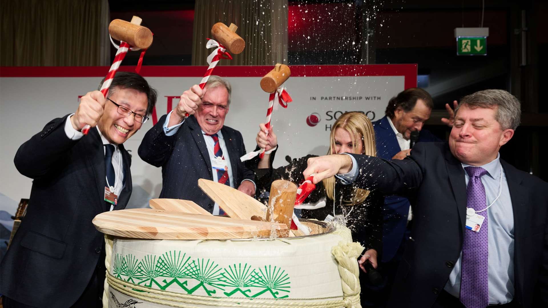 Menschen schlagen bei einem Networking-Event mit Holzhammern auf ein gemeinsames Objekt – ein spielerischer und energiegeladener Moment voller Teamspirit und Interaktion.