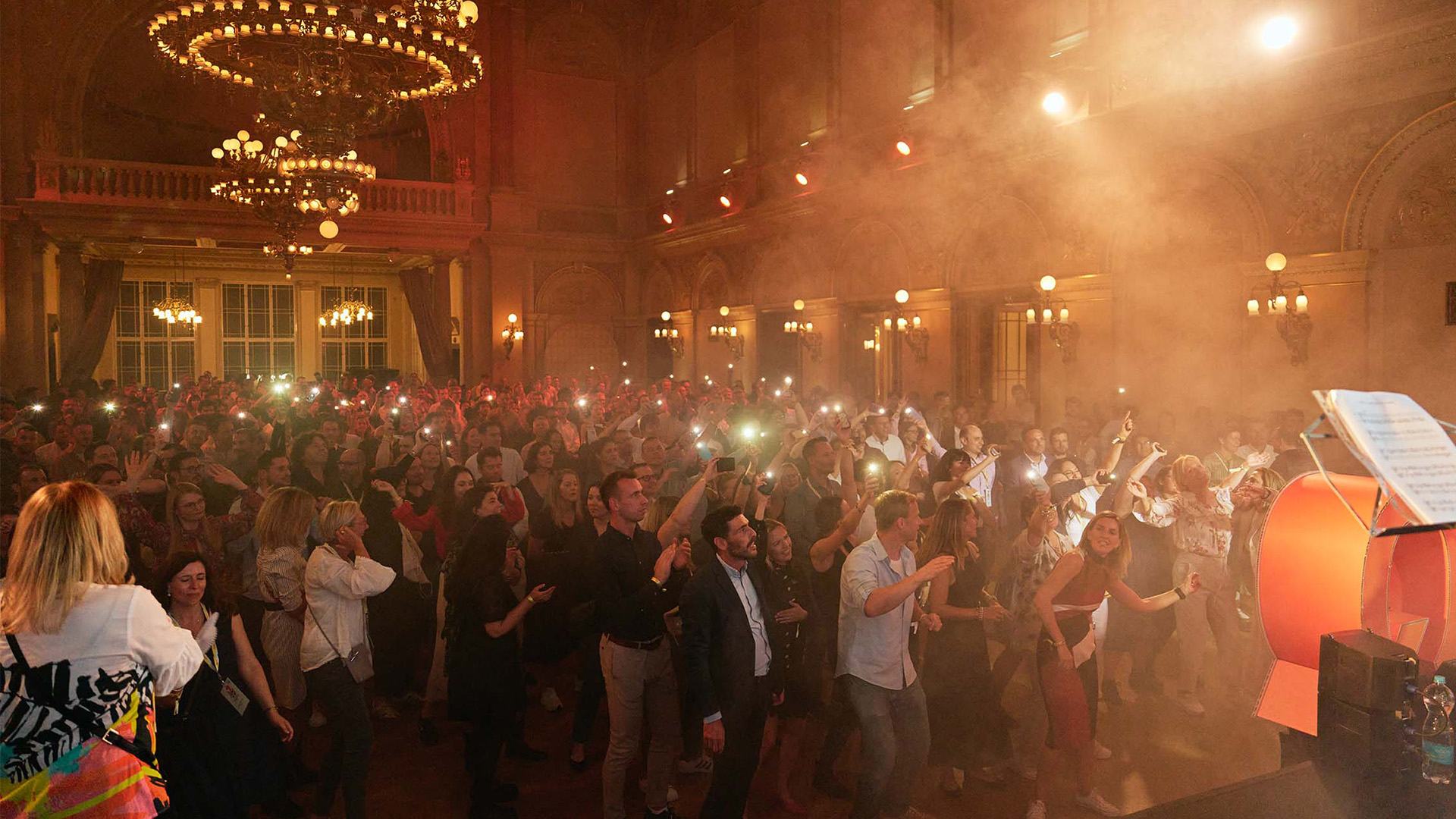Menschen feiern und tanzen bei einem grossen Corporate Event in einem historischen Saal – stimmungsvolle Lichtinszenierung, Live-Moment und starke Gemeinschaftsatmosphäre.