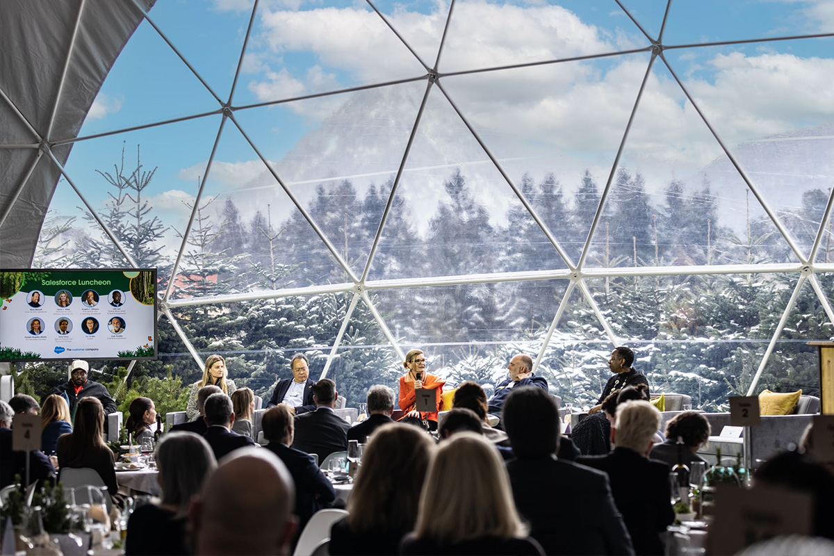 Paneldiskussion während des Salesforce Luncheon in einem transparenten Dome in Davos, mit Blick auf die verschneite Berglandschaft und Gästen an runden Tischen in immersiver Waldatmosphäre.