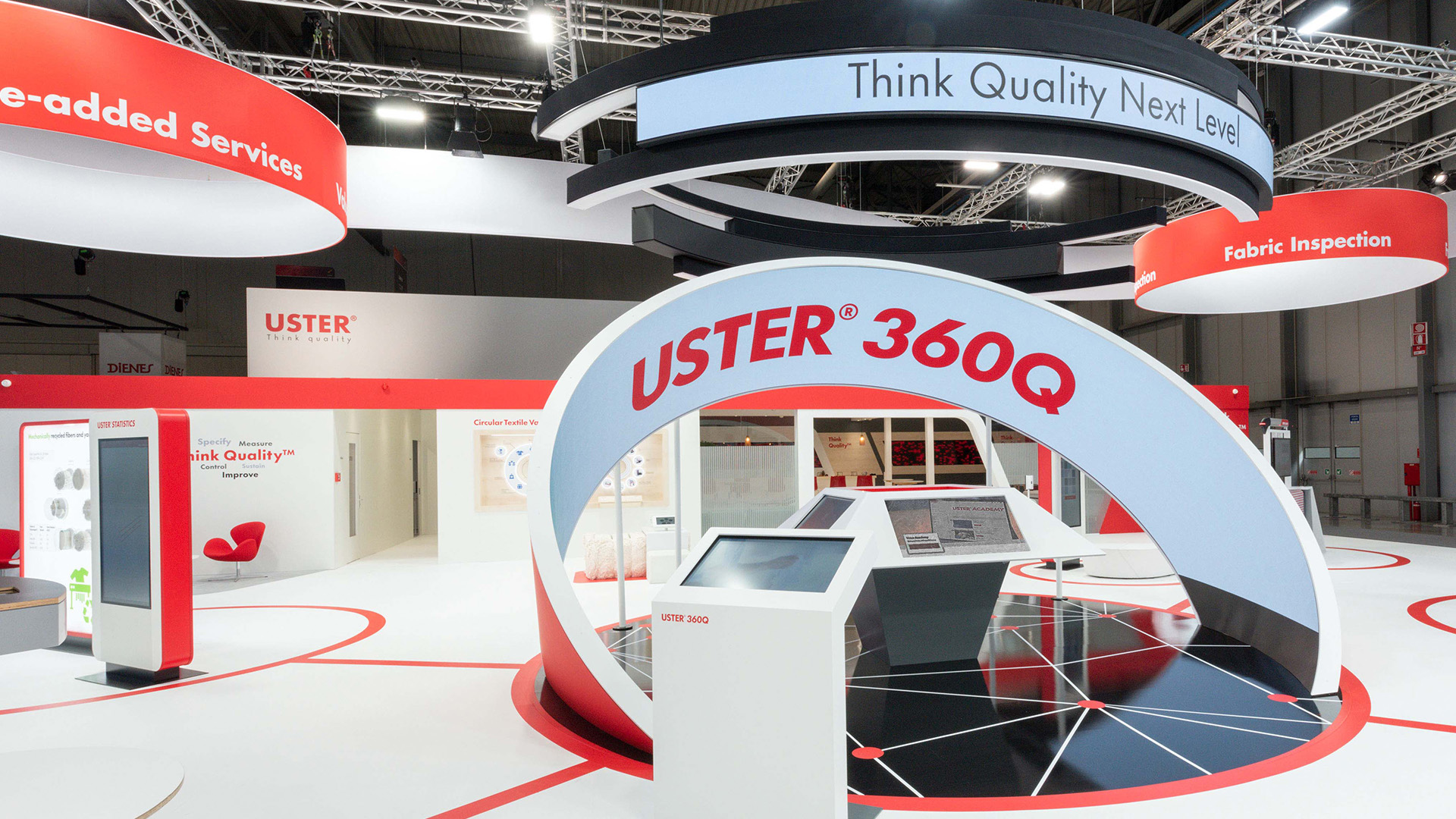 Moderner USTER-Messestand mit „USTER 360Q“-Bogen, interaktiven Displays und futuristischem rot-weiss-schwarzem Design.
