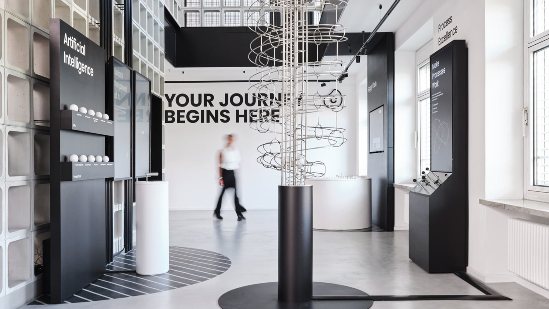 Moderner Erlebnisraum von Celonis mit interaktiven Installationen, digitalen Displays und kinetischer Kugelbahn im minimalistischen Schwarz-Weiss-Design.