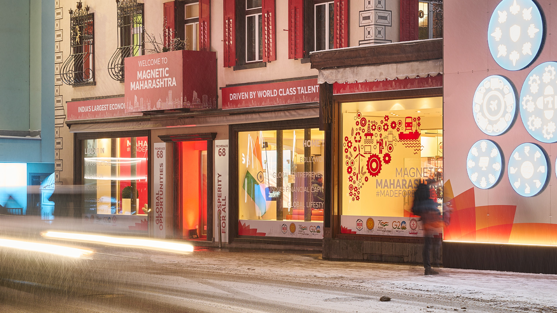 Temporäre Markenlounge in einer winterlichen Einkaufsstrasse, mit beleuchteten Schaufenstern, farbigen Grafiken und vorbeiziehenden Lichtspuren bei Nacht.