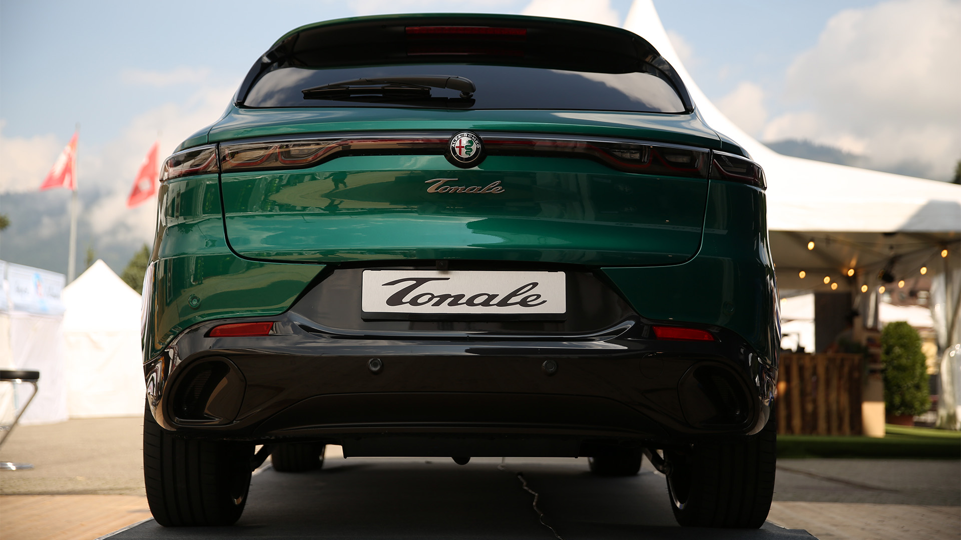 Heckansicht eines grünen Alfa Romeo Tonale auf einer Outdoor-Ausstellungsfläche. Im Hintergrund sind weiße Eventzelte und Schweizer Fahnen vor einer Bergkulisse zu sehen.