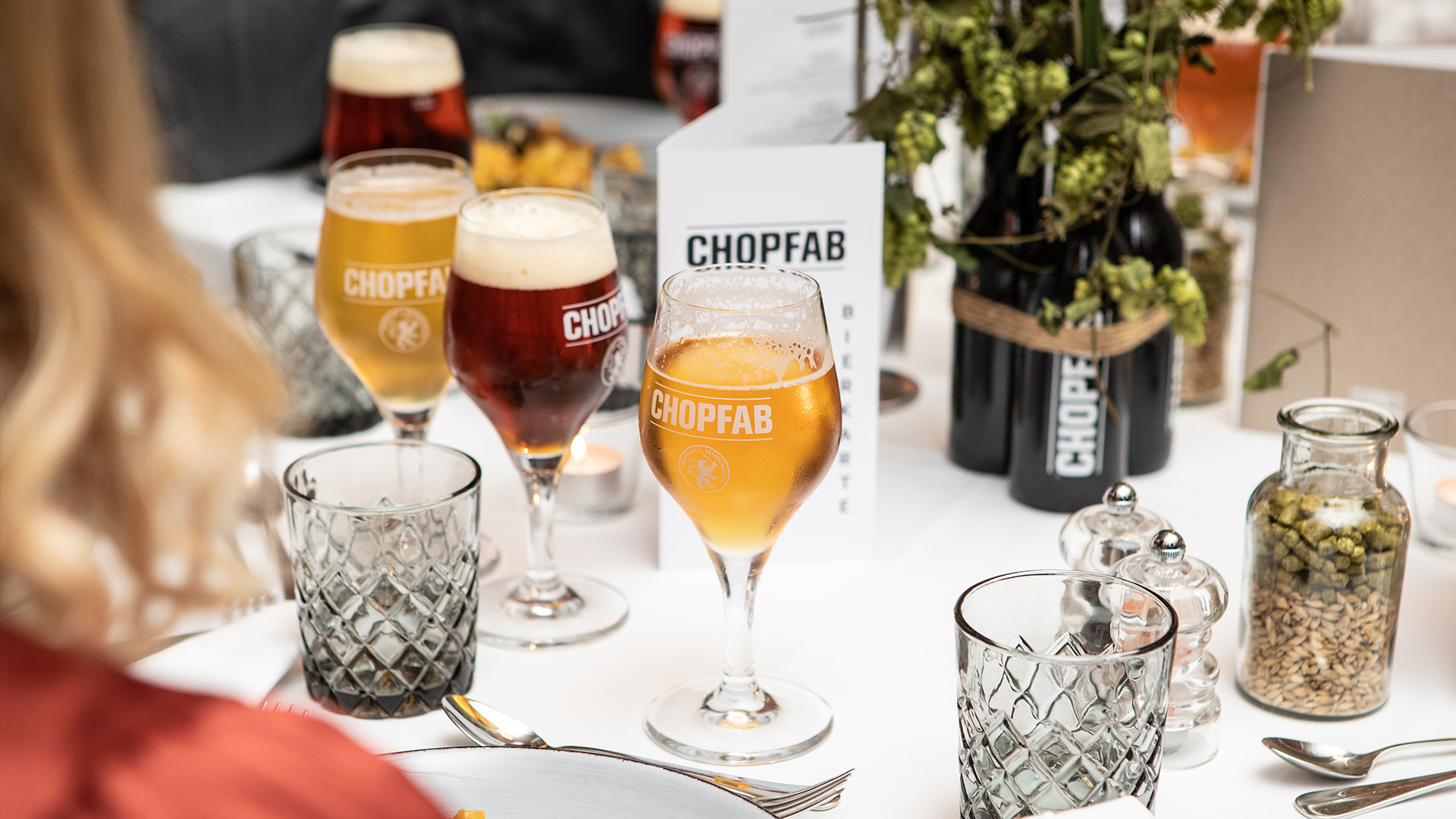 Festlich gedeckter Tisch mit Chopfab-Biergläsern und floraler Dekoration bei einer Jubiläumsveranstaltung.