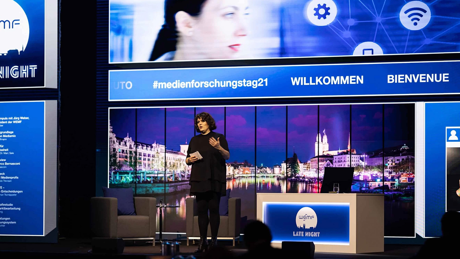 Referentin auf der Bühne des Medienforschungstags vor einer großflächigen digitalen Präsentationswand mit Veranstaltungsbranding.