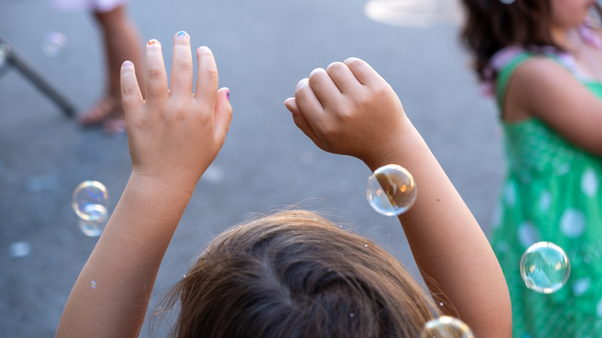 A child with arms raised, surrounded by floating soap bubbles.