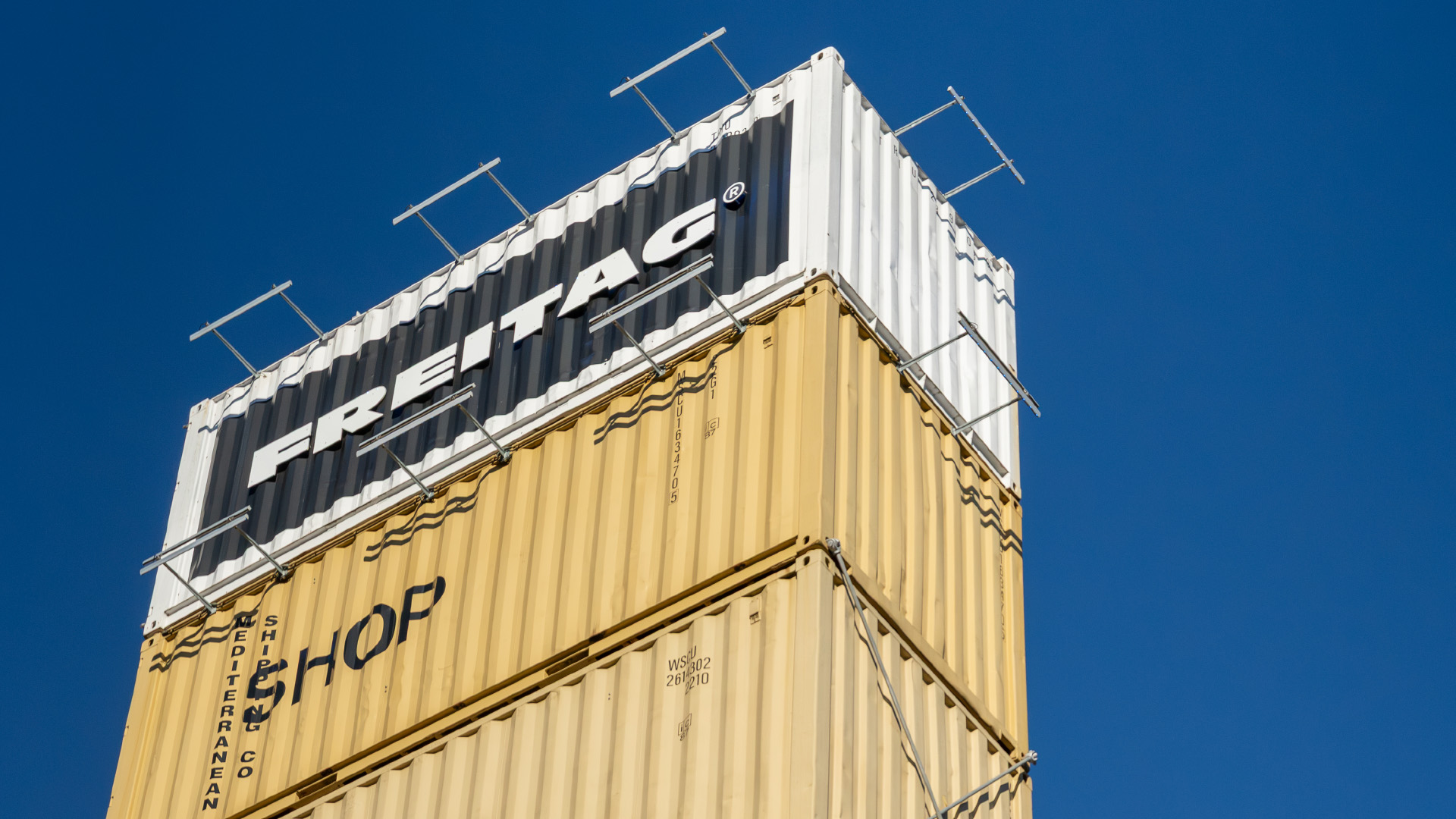 Stacked yellow and white FREITAG containers against a blue sky.