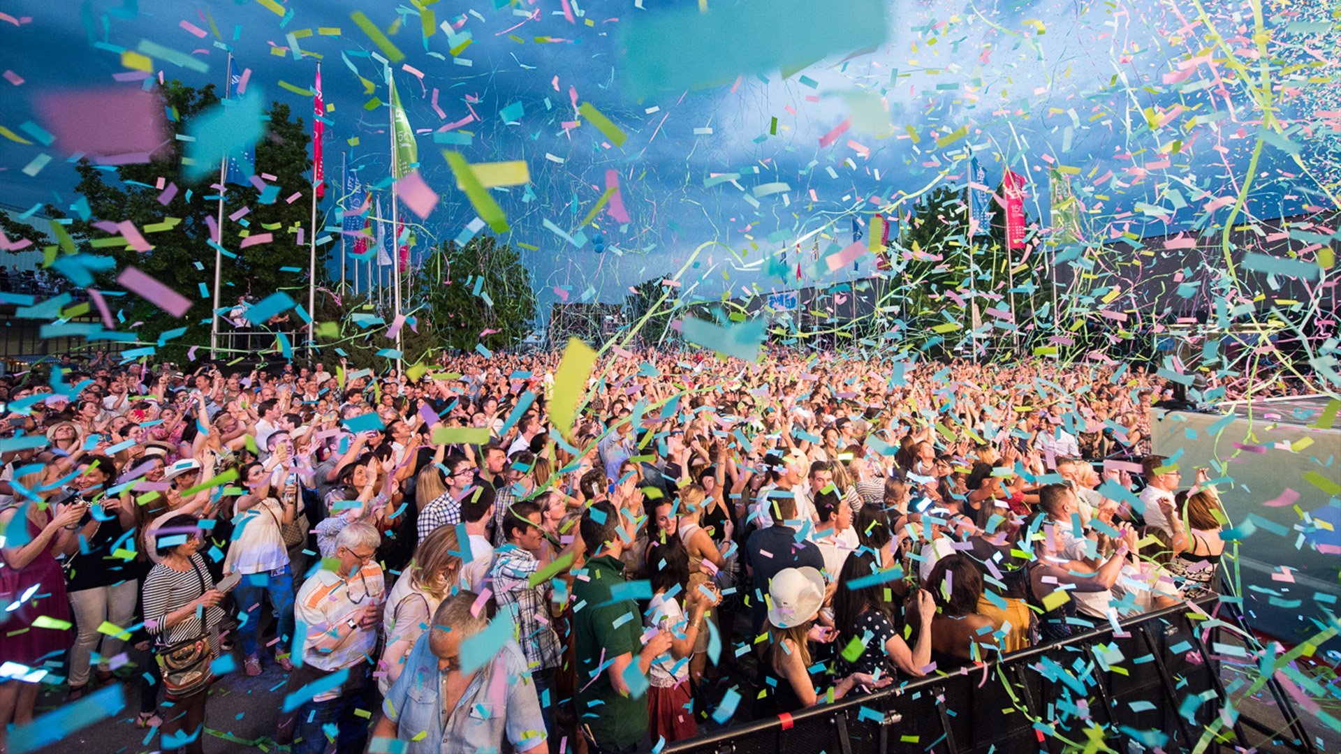 A cheering crowd at an outdoor event, surrounded by a shower of colorful confetti.