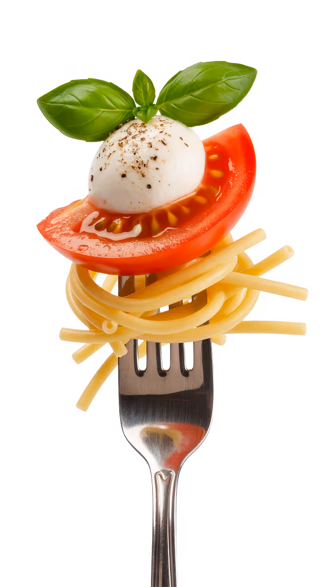 Fork twirling cooked spaghetti topped with a slice of tomato, a ball of mozzarella cheese sprinkled with black pepper, and fresh basil leaves.