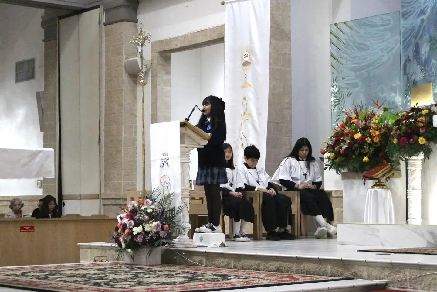 Student speaking at podium during church ceremony with classmates seated nearby