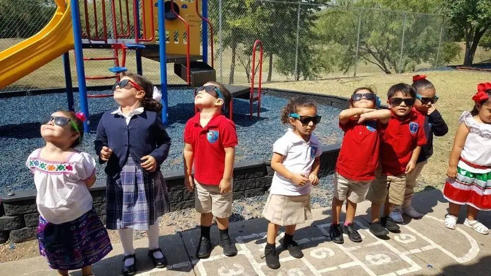 Students wearing eclipse glasses viewing the sky on school playground