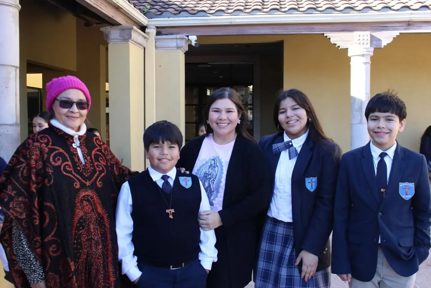 Students and adult visitor smiling together outside school building