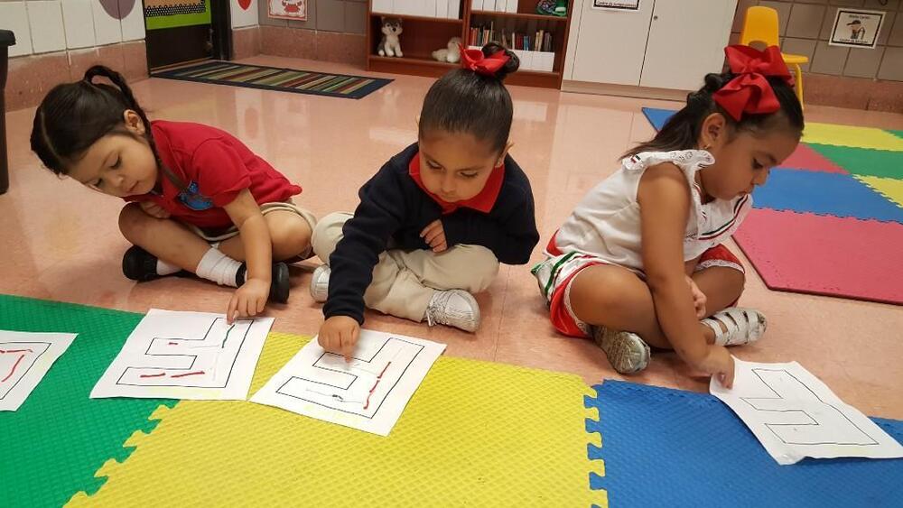 Three young students working on maze worksheets on classroom floor
