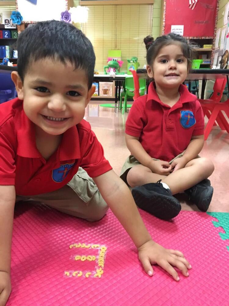 Two students in uniform using cereal to form shapes on classroom floor