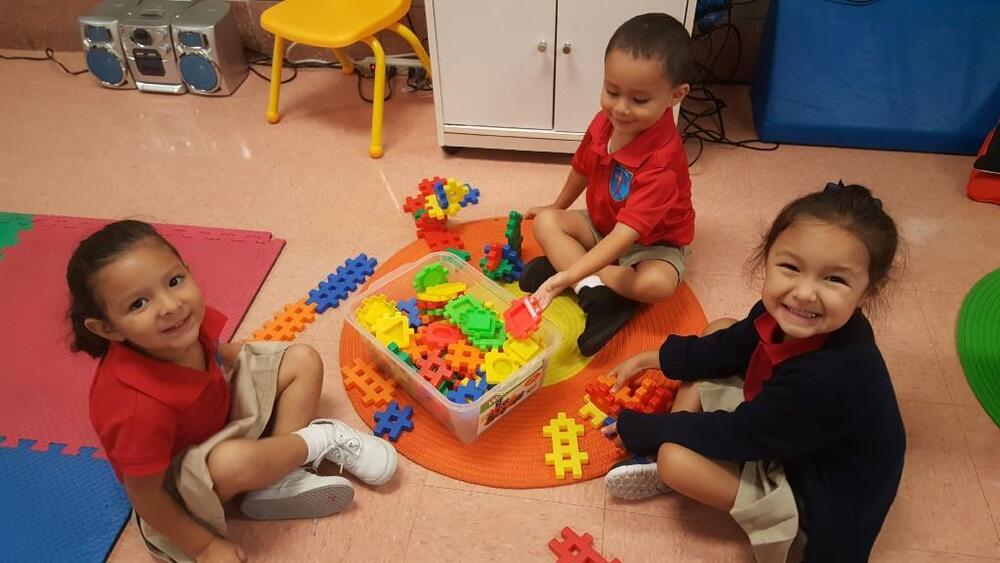 Three young students in uniforms playing with colorful building blocks on classroom floor