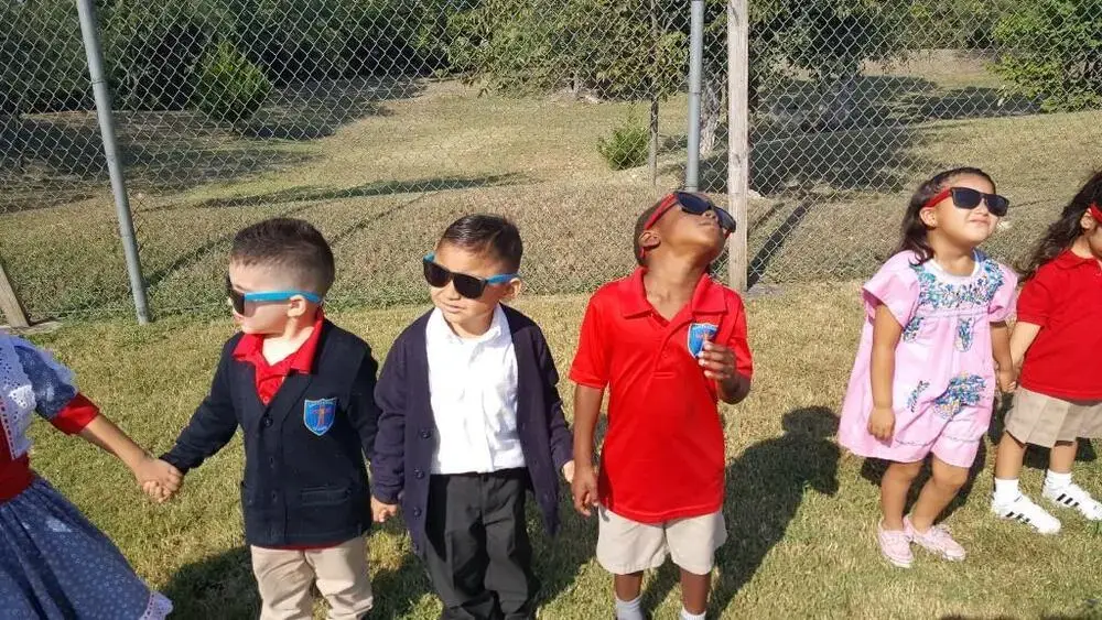 Students wearing eclipse glasses look up at the sky outdoors