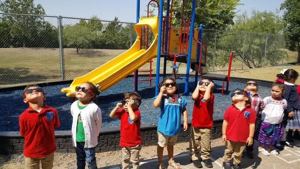 Students wearing eclipse glasses viewing solar eclipse on school playground