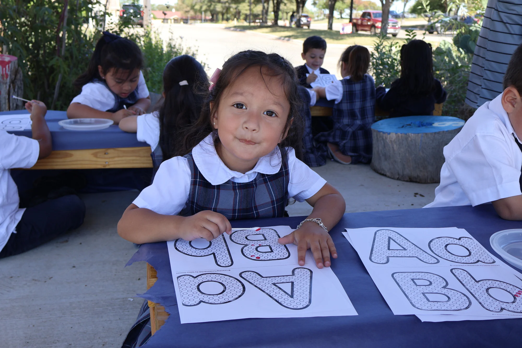 Young student in uniform working on alphabet letter worksheets outdoors