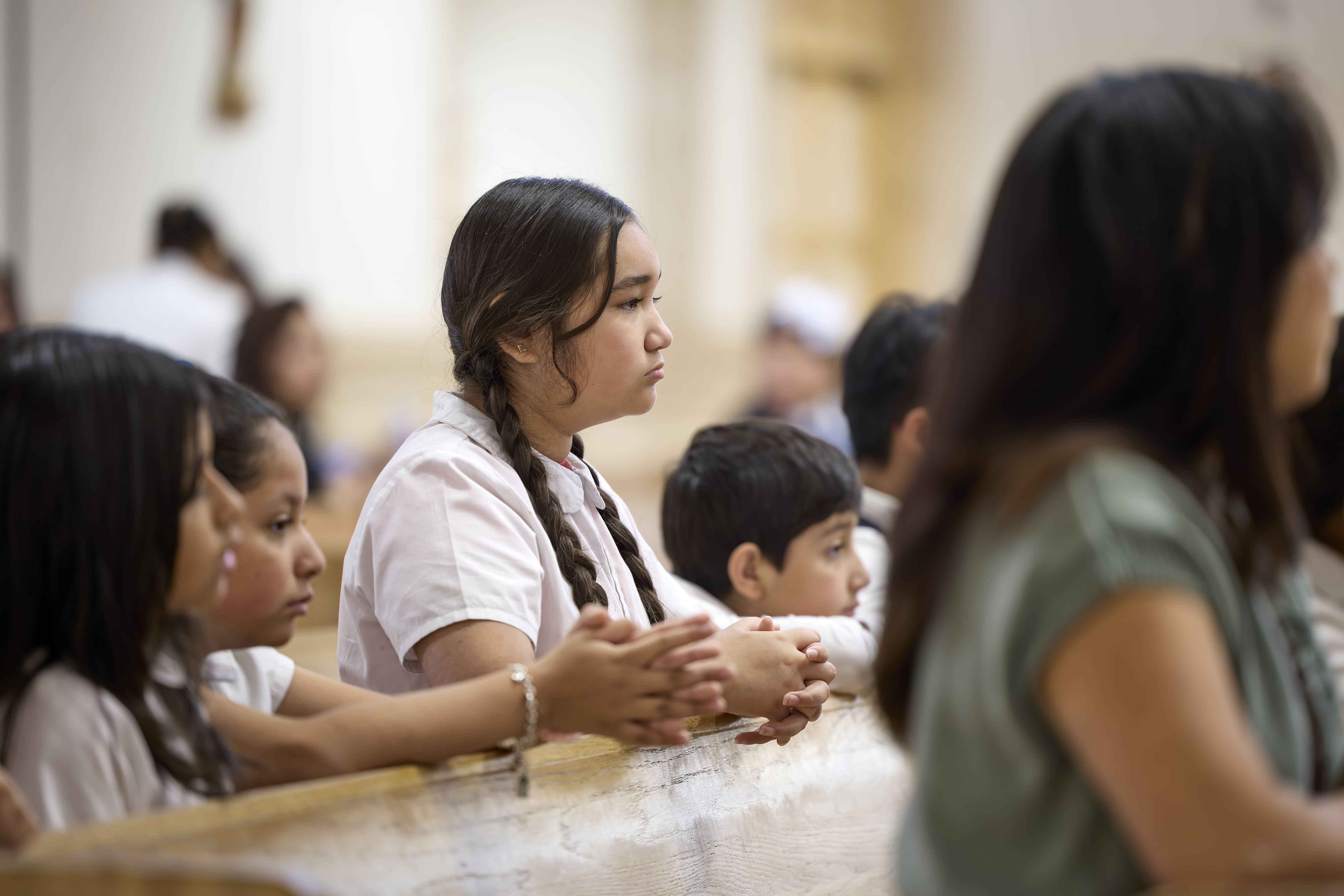 Students in uniform praying reverently in church pews during Mass