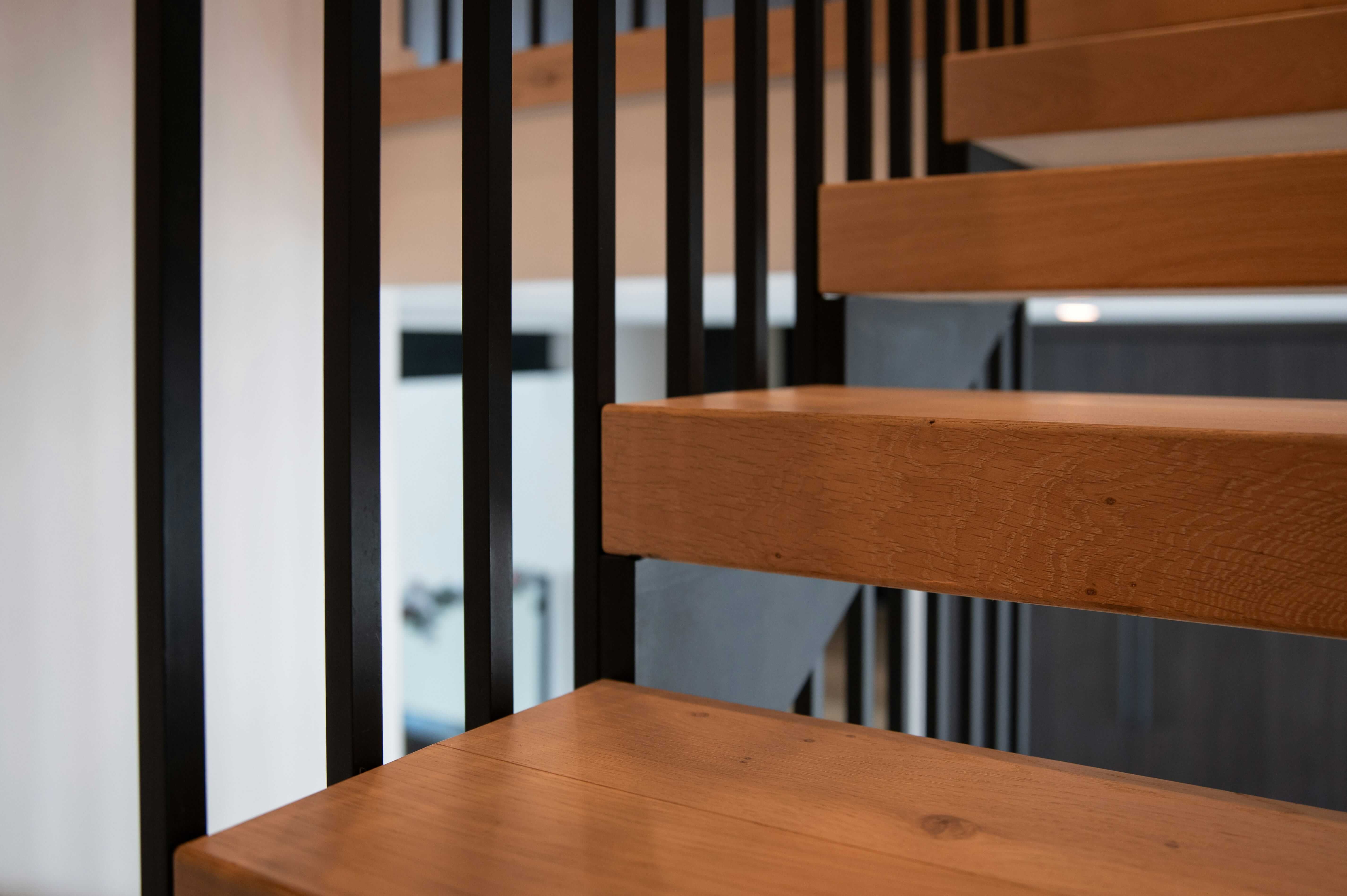 A close-up of a modern architectural staircase with curved railings and beige concrete, against a clear blue sky.