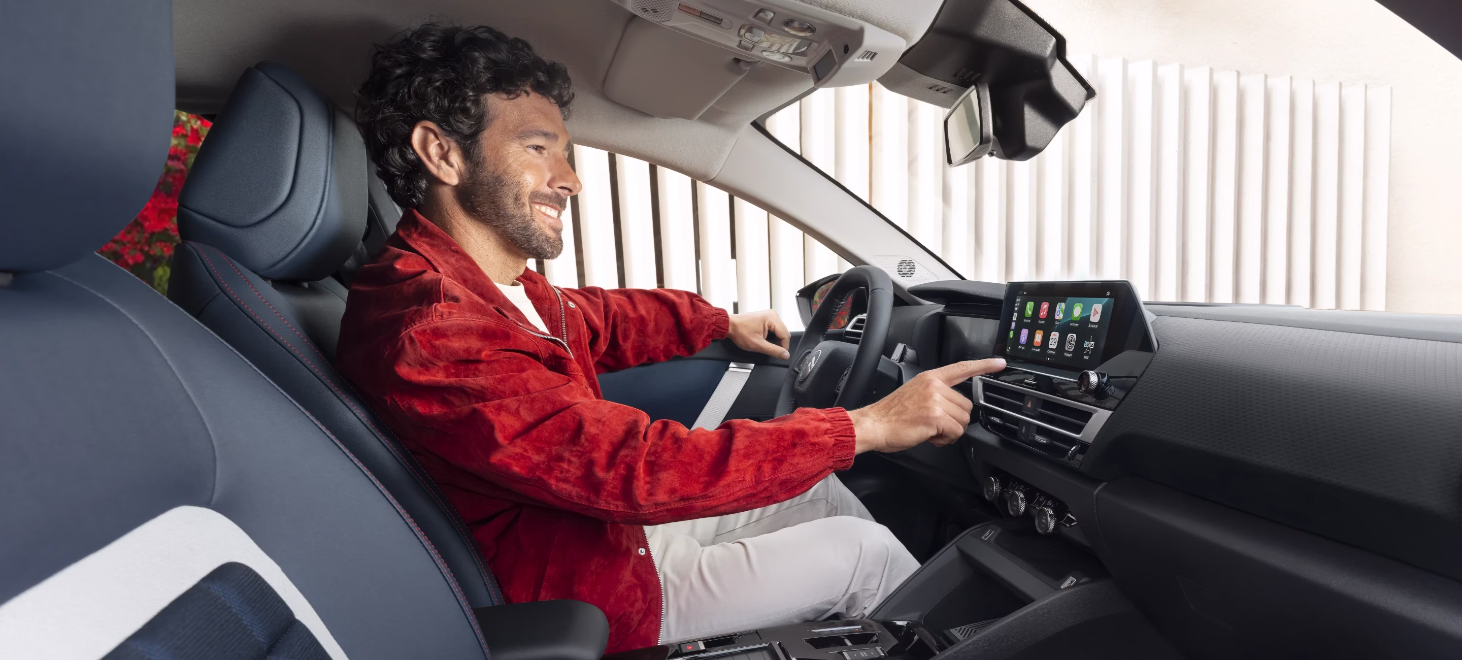 Homme habillé en rouge au volant d'une Citröen touchant le tableau de bord tactile.