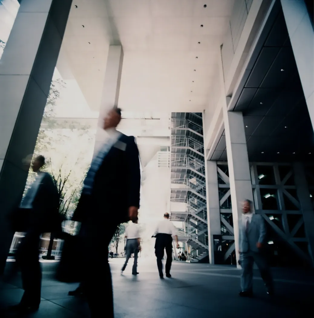 A low angle view of people walking with purpose through an architectural business corridor, representing structured business momentum and disciplined execution.