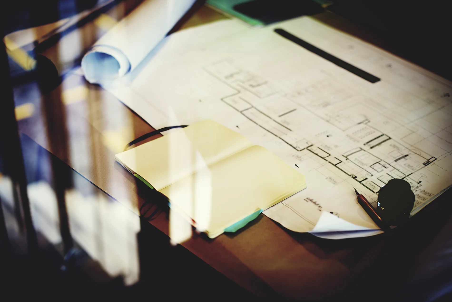 A notebook with a fountain pen sit on top of blueprints, signaling the building of a structured plan