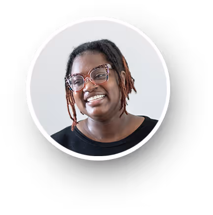 Smiling person with braided hair and patterned glasses wearing a black top against a light background.