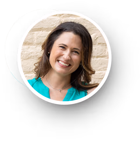 Smiling woman with brown hair wearing a turquoise top against a beige brick wall.