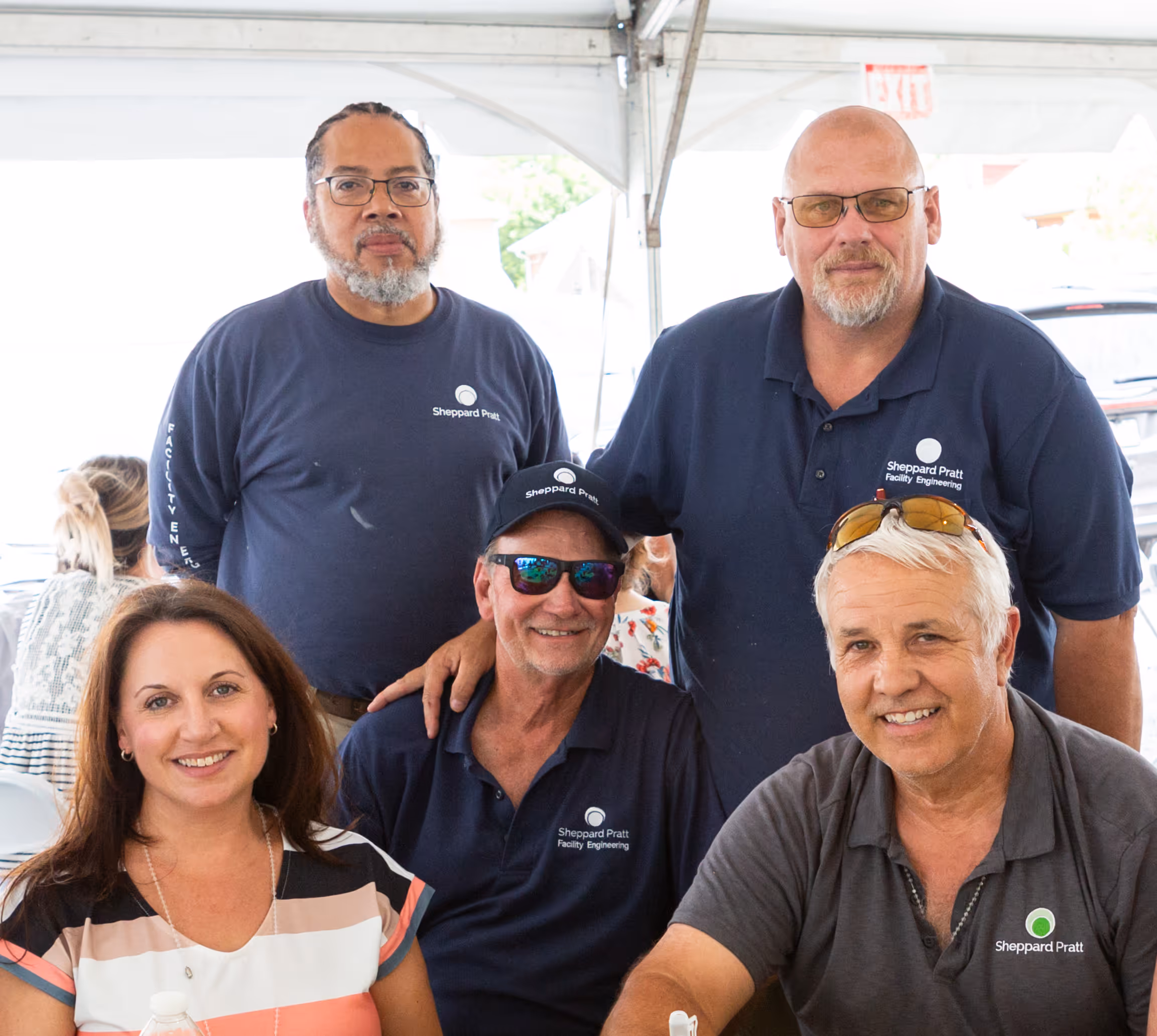 Group of five smiling adults, three men in navy Sheppard Pratt shirts and one woman in striped top.